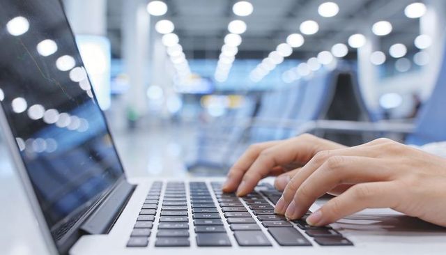 Business traveler typing on laptop at airport gate with bokeh lights and blurred terminal
