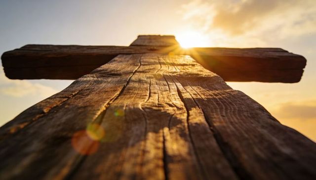 Weathered wooden cross at golden hour backlit with warm sunflare and rustic grain