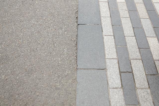 This image shows a clear contrast between a cobblestone walkway and an asphalt road. The textures and patterns of the two surfaces are distinct, making it ideal for use in urban planning presentations, architectural designs, or articles discussing city infrastructure. It can also be used in educational materials about different types of pavement and their uses.