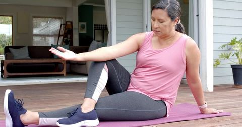Mature woman performing seated spinal twist on porch mat for home fitness and mobility