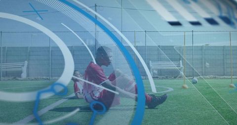 Youth soccer player sitting holding knee on turf during training session with teammate