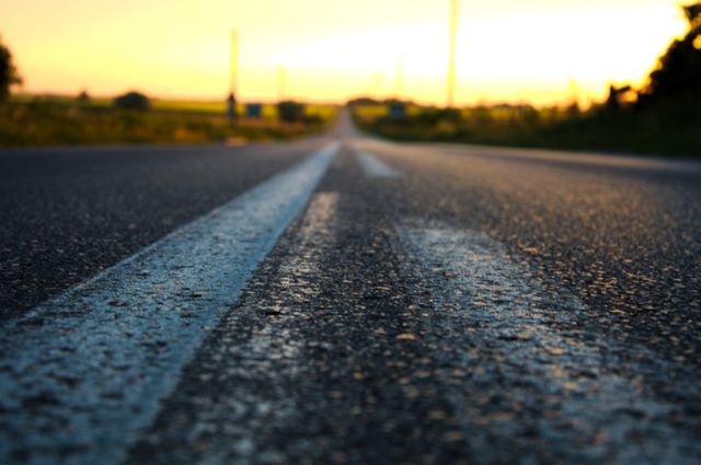 This close-up view of an asphalt road stretching into the sunset offers a feeling of open possibilities and adventure. Perfect for themes related to travel, road trips, and journeys. Useful for backgrounds, motivational posters, or advertisements promoting travel and exploration.