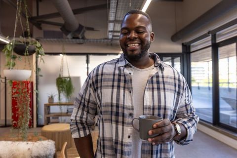 Smiling Professional in Modern Office Lounge Holding Coffee