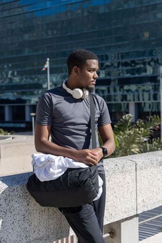 African american man leaning on railing in urban plaza wearing headphones and smartwatch