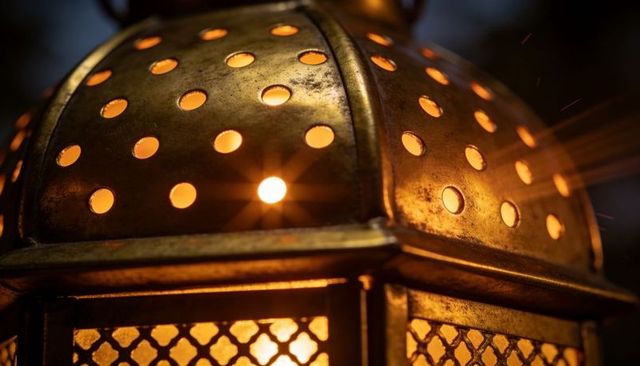 Glowing brass lantern close-up with pierced dome and lattice panels, warm ambient light