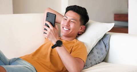 Young Man Relaxing on Sofa with Smartphone and Smartwatch