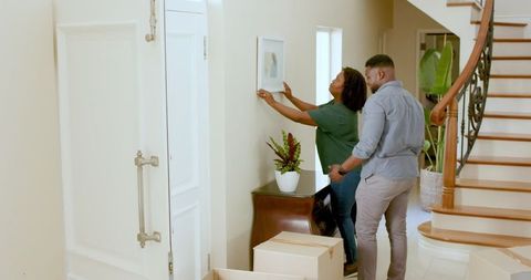 Couple decorating home moving picture near staircase