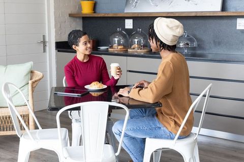 African american couple sipping takeaway coffee, sharing croissant and chatting in cozy cafe