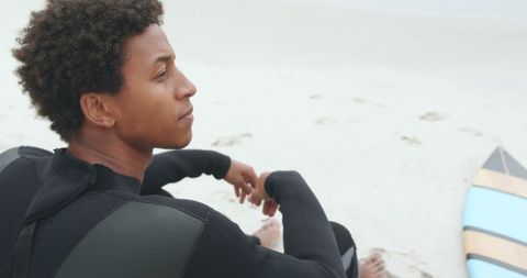 African American Surfer Relaxing on Beach with Surfboard