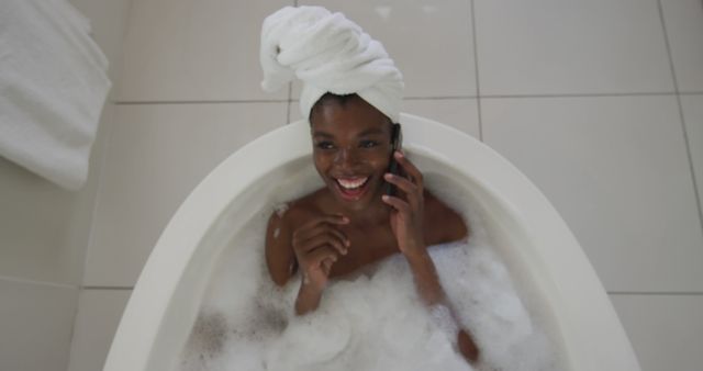 Young woman enjoying a peaceful moment in a bubble bath while talking on the phone. Great for themes on self-care, relaxation, spa day, and personal time. This can be used for advertorials on spa services, wellness blogs, or lifestyle magazines.