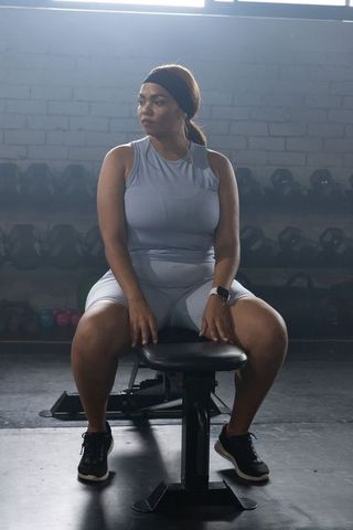 African american woman sitting on bench in gym checking smartwatch after strength training