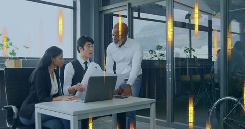 Business team collaborating in modern glass office reviewing documents around laptop