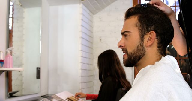 Biracial man sitting in chair and hairdresser touching hair in hair salon, copy space. Indoors, hairdresser, salon, business, proffesionals and beauty unaltered.