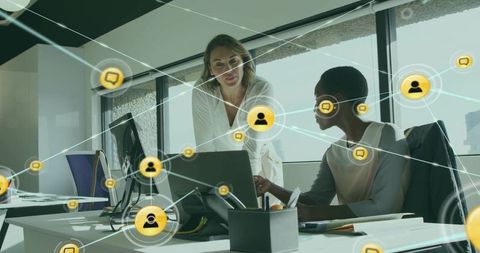 Two Women Collaborating Over Laptop in Modern Office with Digital Network Overlay
