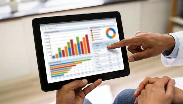 Business colleagues analyzing tablet dashboard with colorful bar and pie charts