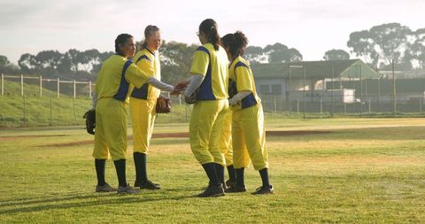 Female softball players huddling on field communicating team strategy