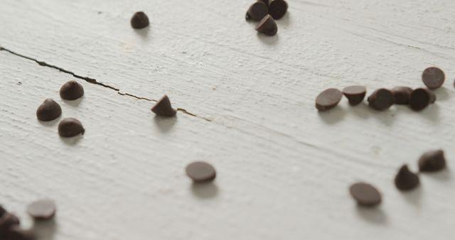 Scatter of chocolate chips over wooden surface conveys a casual, rustic feel perfect for food-related websites, recipe blogs, and culinary magazines. Could be used as an inviting background image for dessert recipes, baking tutorials, ingredient introductions, or promoting chocolate products.
