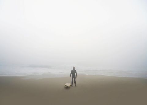 Surfer Braving Misty Beach Morning with Surfboard