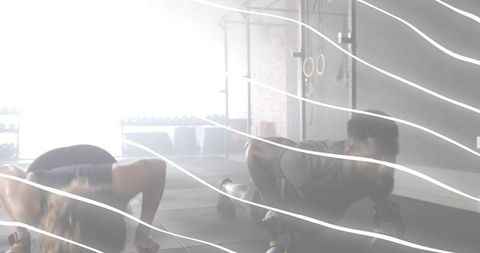 Performing partner push-ups on handles in backlit gym with rings and rack