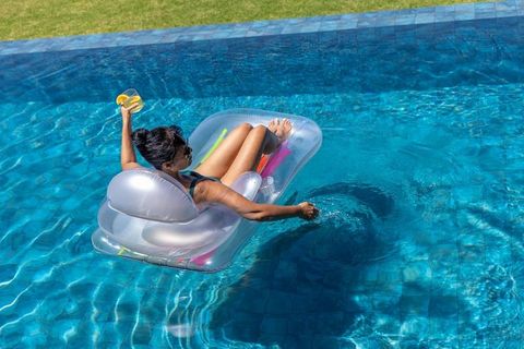 Mature african american woman relaxing on clear pool float holding cocktail in backyard