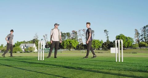 Young men playing casual cricket on green field under clear sky, teamwork and friendship