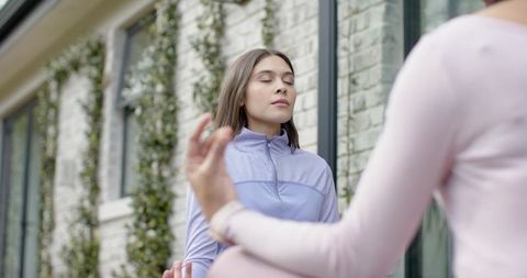 Women meditating outdoors in courtyard by brick wall and vines practicing mindful breathing