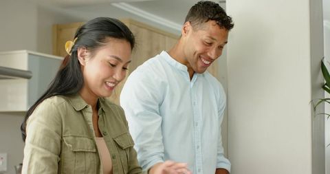 Diverse couple cooking together in modern kitchen, smiling while preparing meal