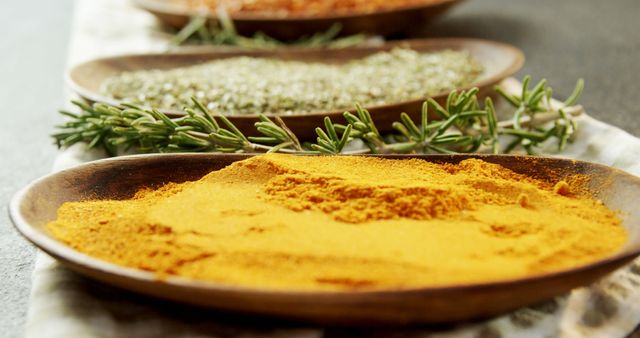 Colorful and aromatic spices and herbs displayed on wooden plates. Turmeric powder is prominent in the foreground, with dried and fresh herbs visible in the background. Ideal for use in culinary blogs, recipe websites, spice and herb store advertisements, or cooking classes.