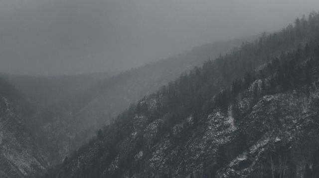 Gloomy fog rolling over snow-covered mountain range, creating mysterious and eerie atmosphere. Perfect for themes relating to nature’s beauty, wilderness exploration, cold weather, and wintertime serenity. Ideal for use in travel blogs, nature documentaries, and landscape photography portfolios.
