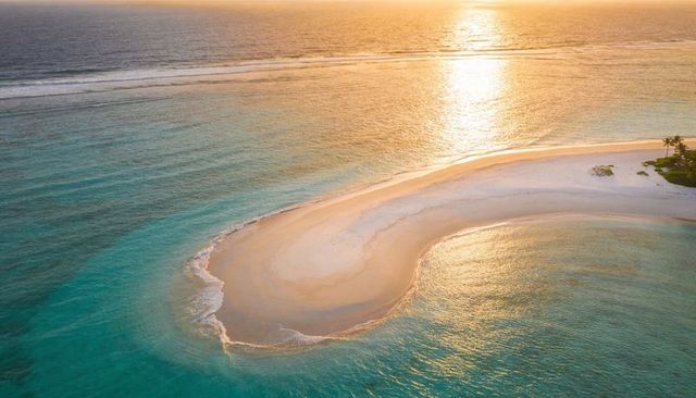 Golden sunset curving sandbar creating crescent lagoon with turquoise water and palms