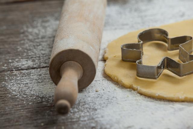 Rolling pin and cookie cutter on dough on wooden surface. Ideal for illustrating baking, holiday preparations, and homemade pastry themes. Perfect for use in cooking blogs, recipe books, and holiday-themed advertisements.