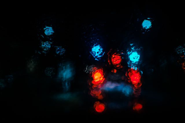 Colorful bokeh lights are seen through a rain-soaked windshield, creating an abstract and artistic look. Useful for backgrounds, wallpapers, and themes related to night driving, rain, or abstract art.