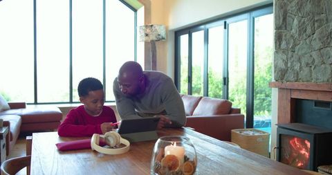 African american father teaching son on tablet at cozy living room table with fireplace