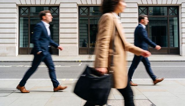 Commuters walking briskly past stone office facade with motion blur and city energy