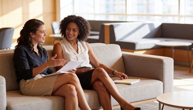 Businesswomen collaborating on lounge couch with notebooks discussing project plans