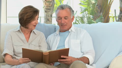 Elderly Couple Reminiscing with Photo Album on Sofa