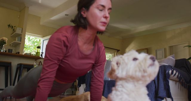 Woman practicing yoga indoors, accompanied by her dog, highlighting a homely and peaceful environment. Ideal for use in blogs, articles, and marketing materials related to wellness, home fitness routines, and companionship with pets.