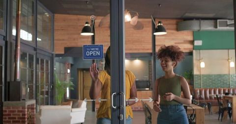 Diverse women entering cozy cafe through glass doors with we are open sign
