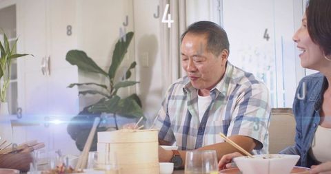Mature man sharing cozy family meal using chopsticks with bamboo steamer and laughter