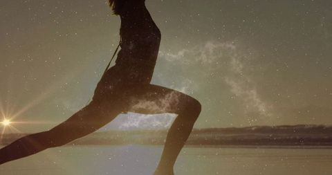 Silhouette female athlete leaping in forward lunge on shoreline at dusk with starfield