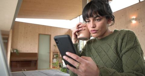 Young woman enjoying coffee break with smartphone in minimalist home workspace