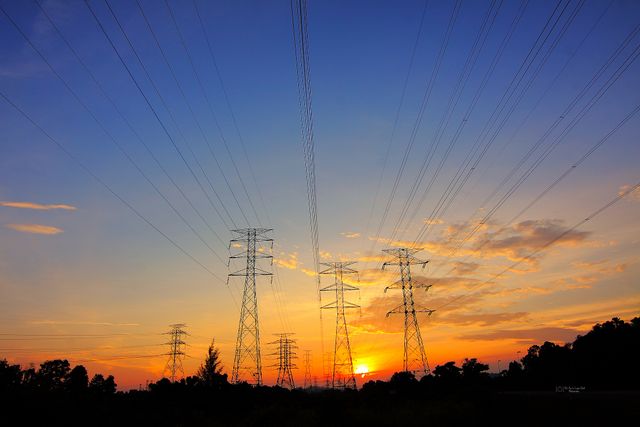 High voltage power lines stretching across the horizon during sunset with a vibrant sky. Perfect for illustrating energy, infrastructure, electricity industry, or environmental themes. It captures the intersection of natural beauty and human engineering.