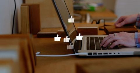 Hands typing on laptop at wood desk with floating social media like icons, cozy coworking