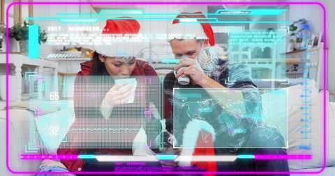Couple wearing santa hats sharing mugs on couch with laptop and futuristic holographic ui