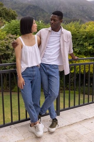 Interracial couple standing and leaning on balcony railing overlooking mountain landscape