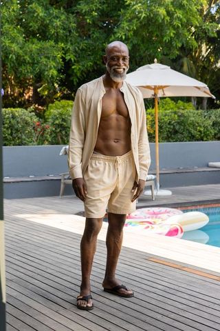 Mature man enjoying poolside afternoon in beige open shirt and shorts, smiling