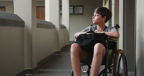 Young boy in wheelchair contemplating school corridor