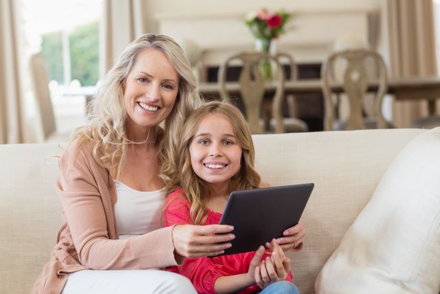Mother and daughter bonding while using a digital tablet on the couch. Perfect for themes related to family, parenting, technology use in households, and modern lifestyle. Ideal for advertisements, blogs, and articles focused on family activities, digital learning, and home leisure.