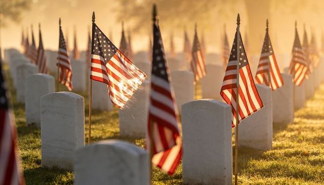 American flags marking military graves at sunrise in symmetrical memorial cemetery