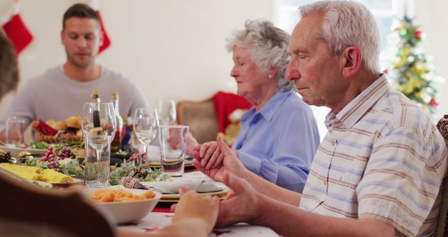 Caucasian family having christmas dinner. sitting on dining table holding hands and praying together before having lunch during christmas at home. christmas festivity celebration tradition